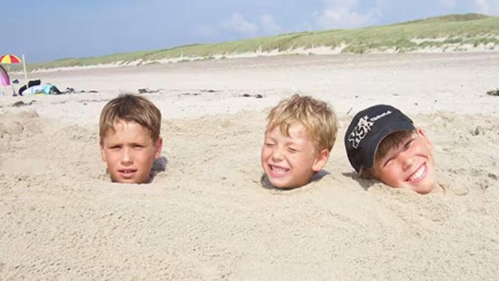 Tre drenge hoveder, der stikker op af sandet på en strand