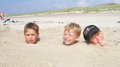 Tre drenge hoveder, der stikker op af sandet på en strand